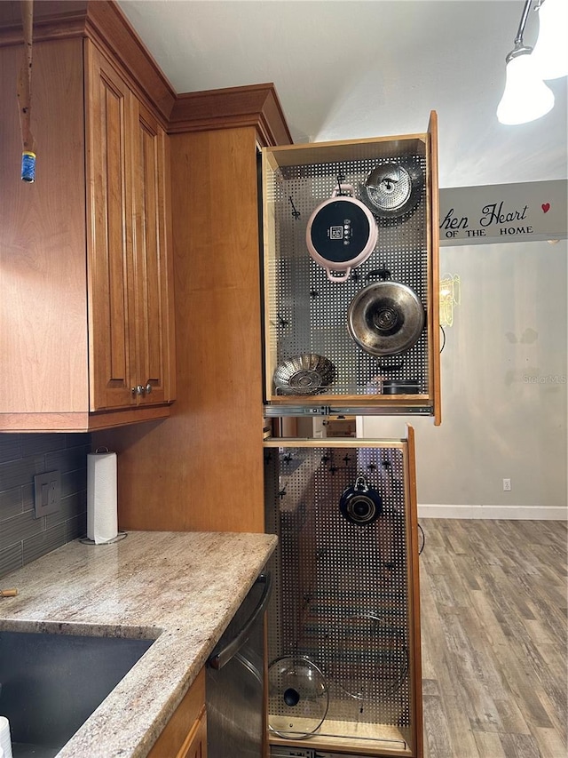 kitchen with light stone counters, decorative light fixtures, light hardwood / wood-style floors, backsplash, and black dishwasher