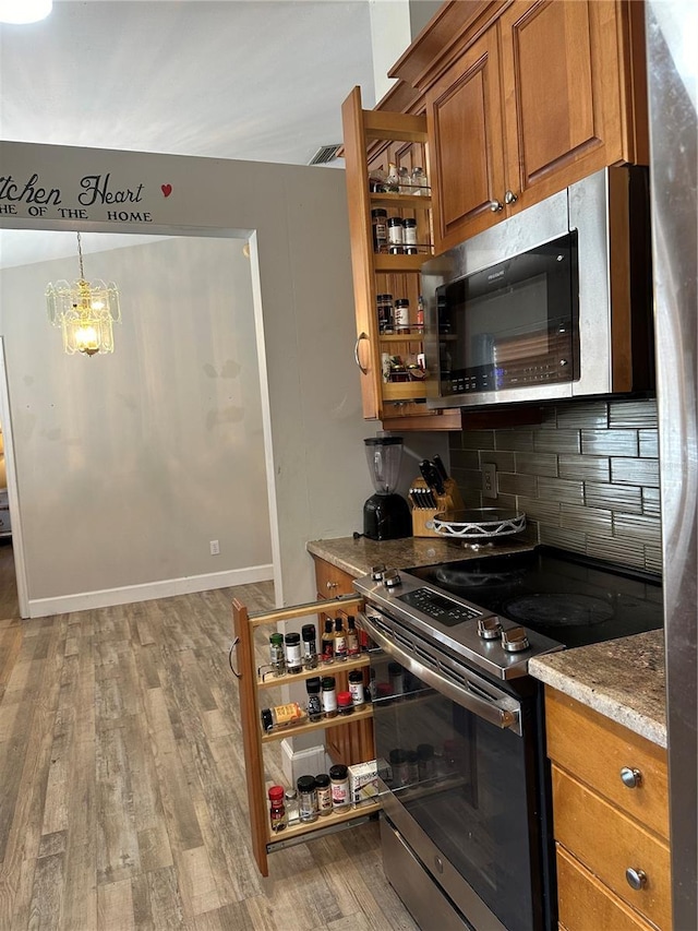 kitchen with a chandelier, appliances with stainless steel finishes, hanging light fixtures, light hardwood / wood-style floors, and decorative backsplash