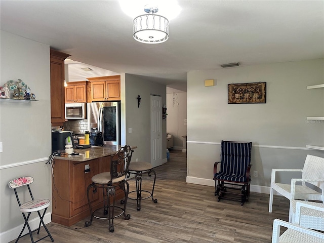 kitchen featuring dark wood-type flooring, a breakfast bar, decorative backsplash, dark stone counters, and appliances with stainless steel finishes