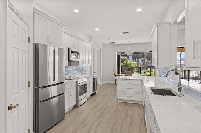 kitchen with appliances with stainless steel finishes, backsplash, sink, white cabinets, and hanging light fixtures