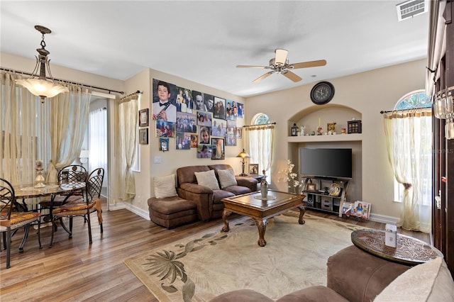 living room featuring built in shelves, ceiling fan, and light hardwood / wood-style floors