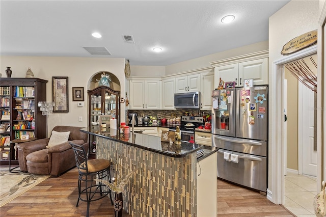 kitchen featuring a breakfast bar, dark stone counters, light hardwood / wood-style flooring, appliances with stainless steel finishes, and white cabinetry