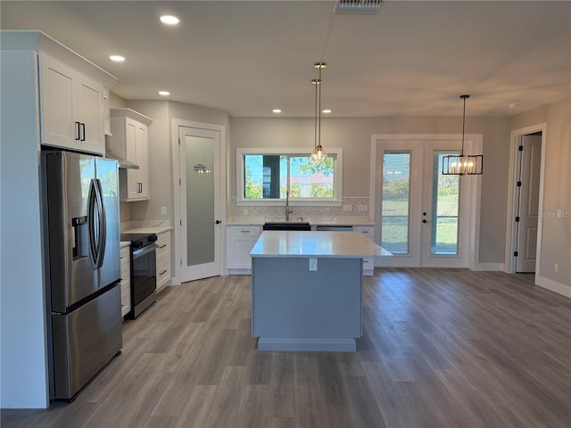 kitchen with range with electric stovetop, stainless steel refrigerator with ice dispenser, hanging light fixtures, and white cabinets