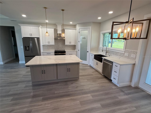 kitchen with white cabinetry, appliances with stainless steel finishes, a kitchen island, and wall chimney range hood