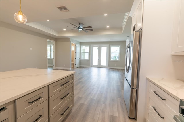 kitchen with french doors, hanging light fixtures, stainless steel fridge, a raised ceiling, and light stone countertops