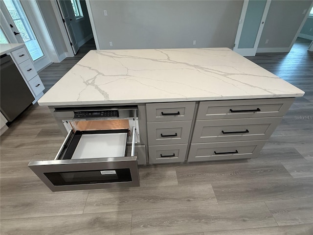 kitchen with gray cabinets, a kitchen island, dishwashing machine, dark hardwood / wood-style flooring, and light stone countertops