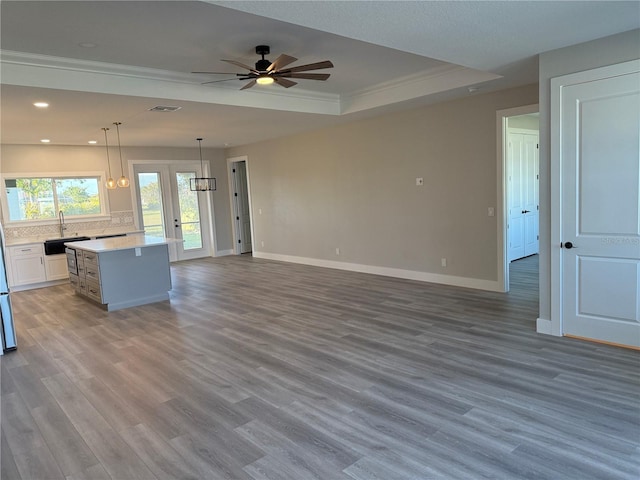 unfurnished living room with sink, crown molding, a tray ceiling, ceiling fan, and hardwood / wood-style floors