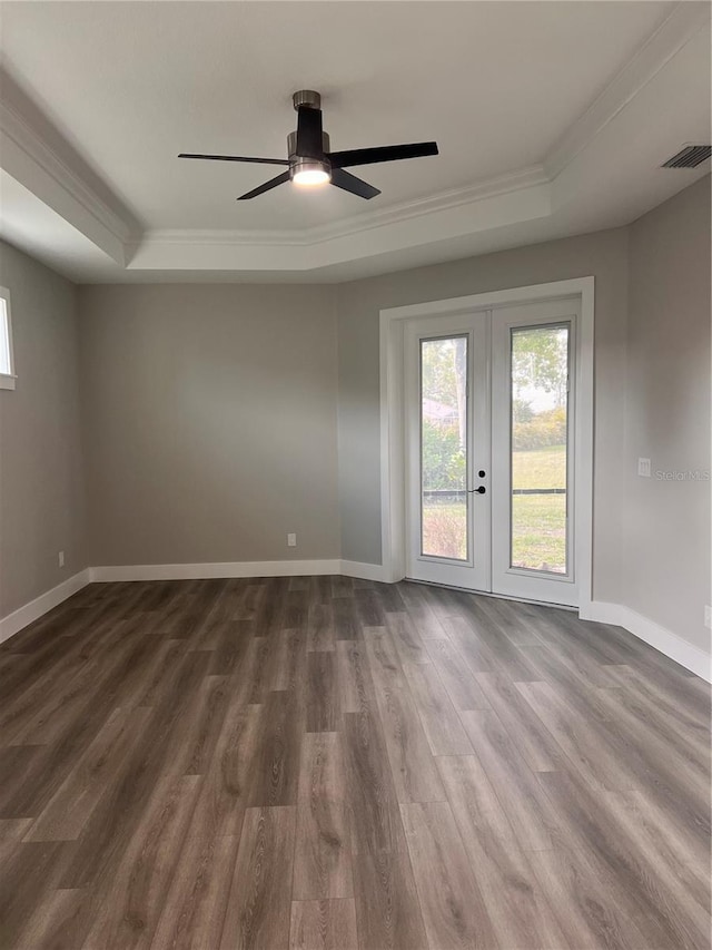 unfurnished room with ceiling fan, a tray ceiling, ornamental molding, dark hardwood / wood-style flooring, and french doors