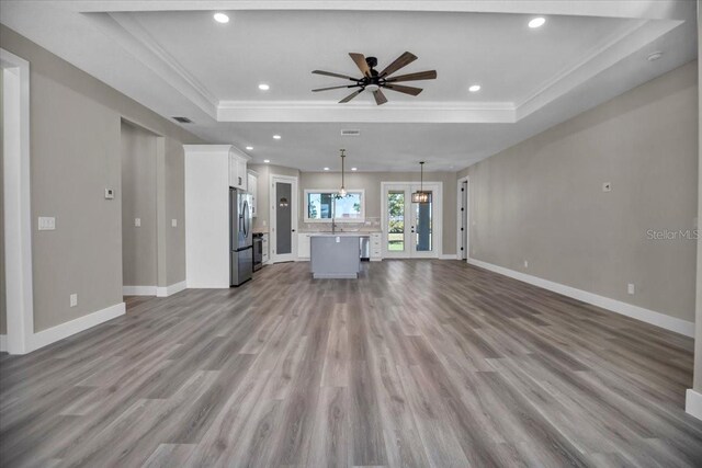 unfurnished living room featuring a raised ceiling, baseboards, and wood finished floors