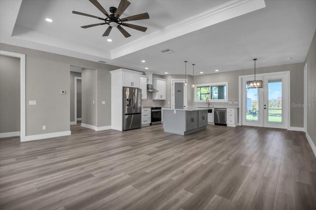 unfurnished living room featuring a sink, baseboards, a tray ceiling, and wood finished floors