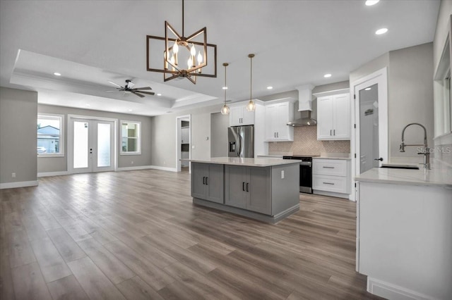 kitchen with a tray ceiling, a center island, backsplash, appliances with stainless steel finishes, and wall chimney exhaust hood