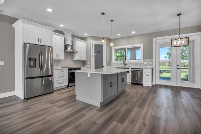 kitchen featuring stainless steel appliances, white cabinets, light countertops, and wall chimney range hood