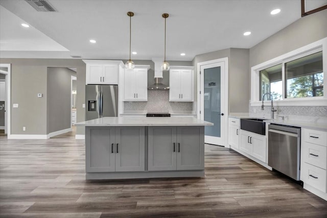 kitchen with a sink, visible vents, appliances with stainless steel finishes, a center island, and wall chimney exhaust hood