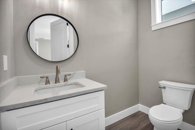 bathroom with toilet, baseboards, wood finished floors, and vanity