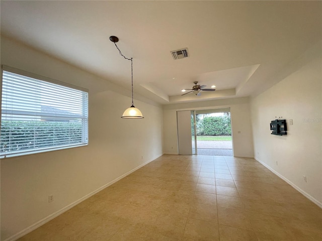 tiled spare room featuring a raised ceiling and ceiling fan