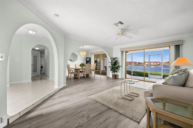 living room featuring wood-type flooring, ceiling fan with notable chandelier, a water view, and a textured ceiling