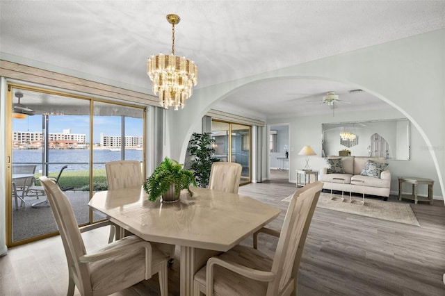 dining area featuring a textured ceiling, a water view, ceiling fan with notable chandelier, and light wood-type flooring