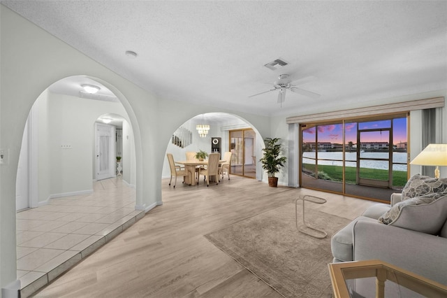 living room with ceiling fan with notable chandelier, a water view, light hardwood / wood-style floors, and a textured ceiling