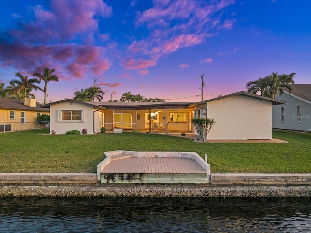 back house at dusk with a yard and a water view