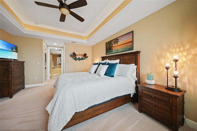 carpeted bedroom with a raised ceiling, connected bathroom, and ceiling fan