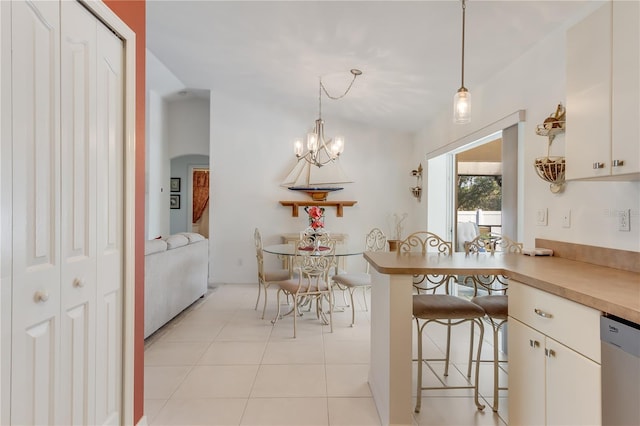 kitchen with a breakfast bar, light tile patterned floors, decorative light fixtures, dishwasher, and white cabinetry