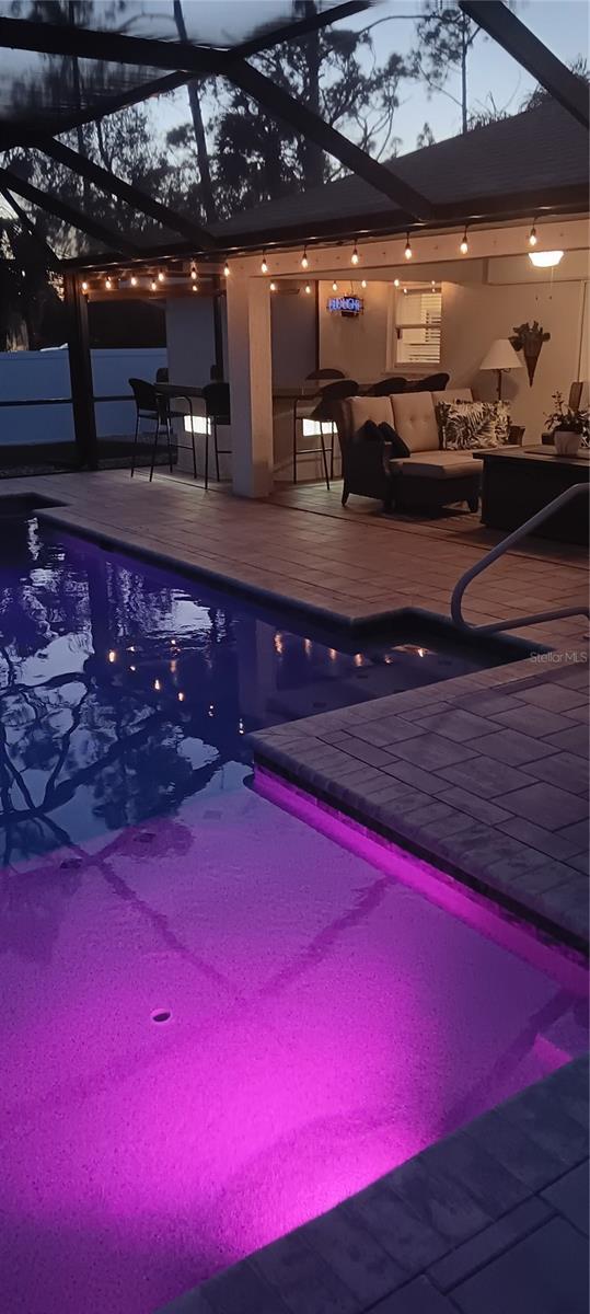 pool at dusk with glass enclosure, an outdoor hangout area, and a patio