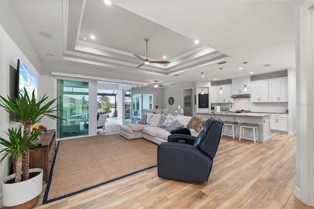 living room featuring ceiling fan, sink, light wood-type flooring, and a tray ceiling