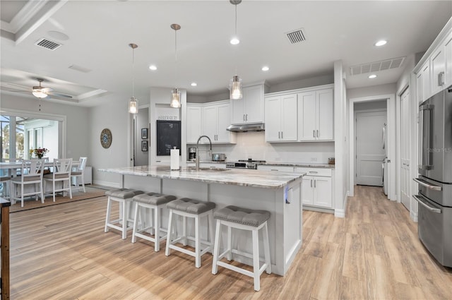 kitchen with high end fridge, a center island with sink, white cabinets, and decorative light fixtures