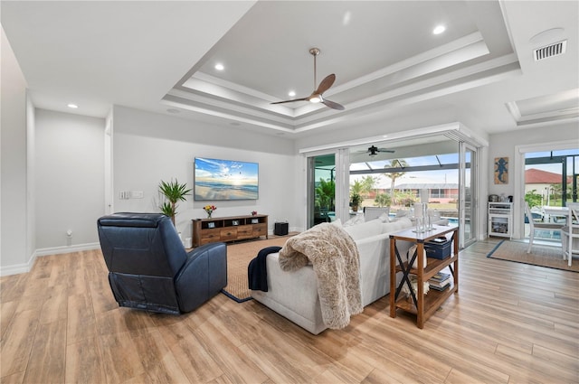 living room with ceiling fan, a raised ceiling, and light hardwood / wood-style flooring