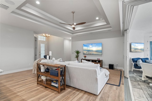 living room with ceiling fan, ornamental molding, a tray ceiling, and light wood-type flooring