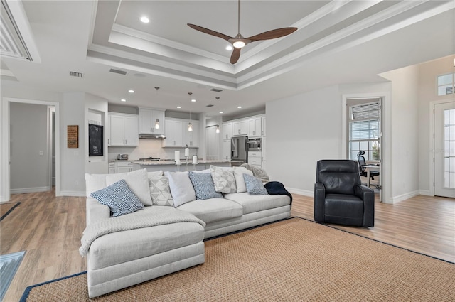 living room featuring a raised ceiling, crown molding, ceiling fan, and light hardwood / wood-style floors