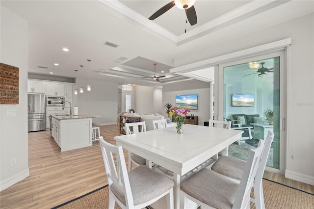 dining space with sink, ceiling fan, a raised ceiling, crown molding, and light hardwood / wood-style flooring