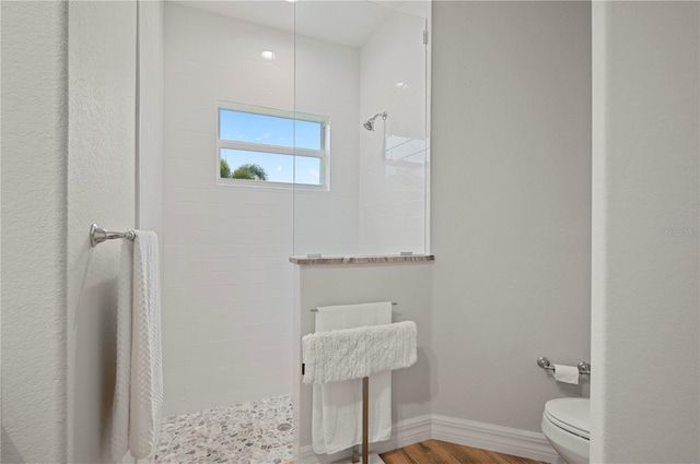 bathroom featuring toilet, hardwood / wood-style floors, and a tile shower