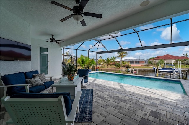 view of swimming pool featuring ceiling fan, a patio, glass enclosure, a water view, and an outdoor living space