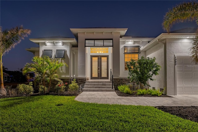 exterior entry at twilight featuring a garage and a lawn