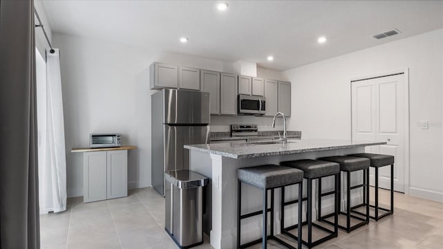 2784 Dode Ave, North Port, FL 34288 - kitchen with appliances with stainless steel finishes, gray cabinets, light stone countertops, a breakfast bar area, and a kitchen island with sink