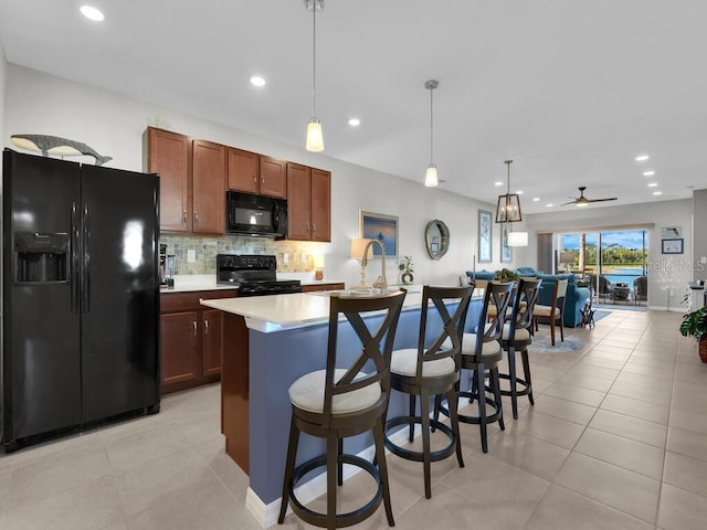 kitchen with ceiling fan, black appliances, pendant lighting, light tile patterned floors, and a center island with sink