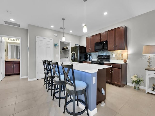 kitchen with backsplash, pendant lighting, a breakfast bar, black appliances, and a center island with sink