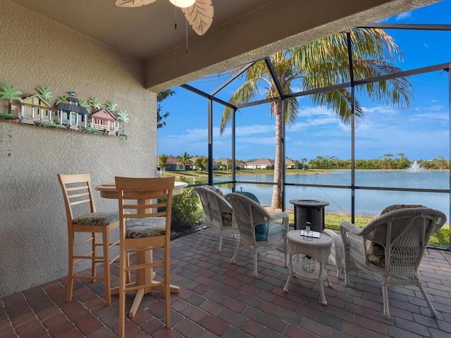 view of patio with a water view, glass enclosure, and ceiling fan