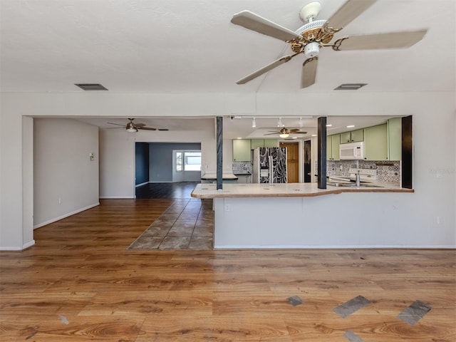 kitchen featuring green cabinetry, refrigerator with ice dispenser, decorative backsplash, stove, and kitchen peninsula