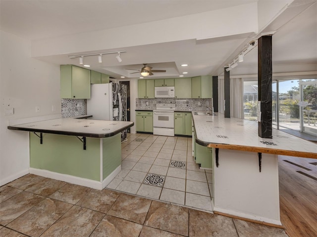 kitchen featuring green cabinets, white appliances, a kitchen breakfast bar, and kitchen peninsula