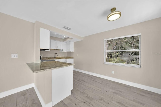 kitchen featuring white cabinetry, sink, light stone counters, kitchen peninsula, and light wood-type flooring