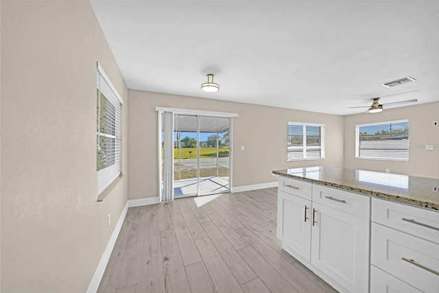 kitchen with white cabinets, light hardwood / wood-style floors, ceiling fan, and dark stone countertops