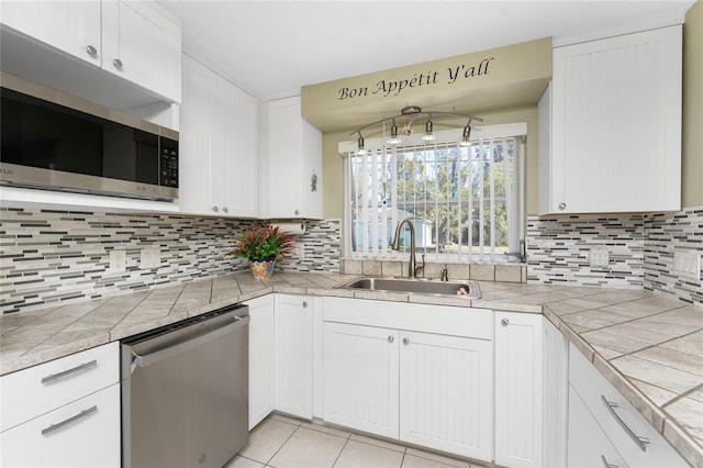 kitchen with tile counters, sink, white cabinets, and appliances with stainless steel finishes