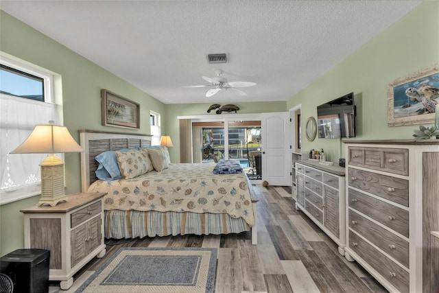 bedroom with ceiling fan, access to exterior, a textured ceiling, and hardwood / wood-style floors