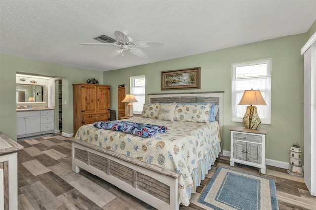 bedroom with ceiling fan, connected bathroom, hardwood / wood-style flooring, and a textured ceiling