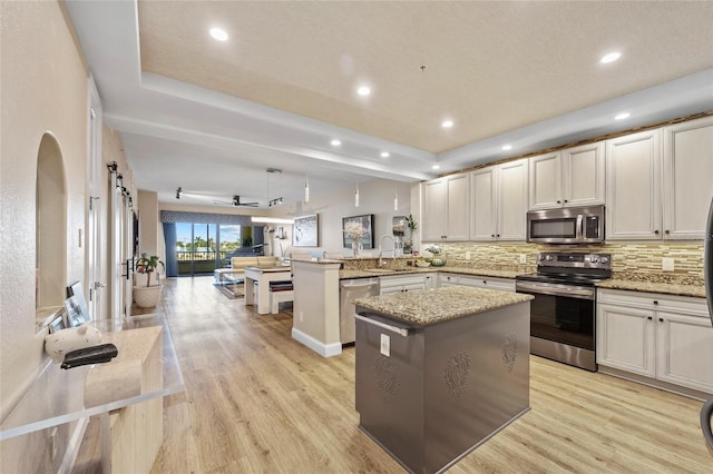 kitchen with kitchen peninsula, appliances with stainless steel finishes, tasteful backsplash, decorative light fixtures, and light hardwood / wood-style flooring