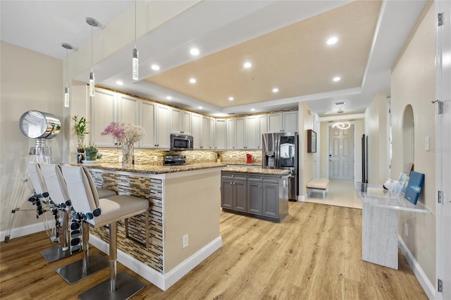 kitchen with gray cabinets, kitchen peninsula, a kitchen bar, hanging light fixtures, and stainless steel appliances