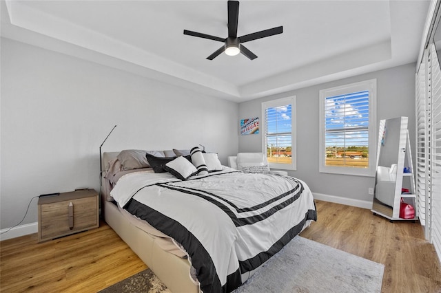 bedroom with a raised ceiling, ceiling fan, and light wood-type flooring