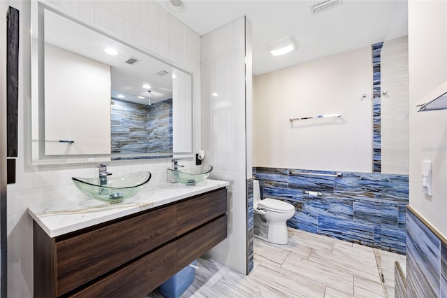 bathroom featuring toilet, vanity, and tile walls